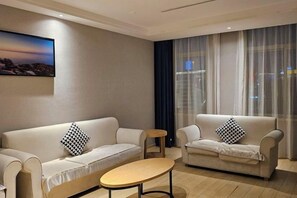 A modern living room with two sofas, a small round table, and a cityscape view through large windows. - Kyriad Marvclous Hotel Dongguan Nancheng International Trade Center (Dongguan)