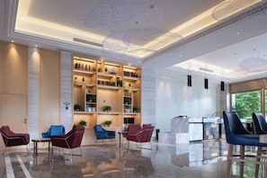 A modern lobby with a reception desk, seating area, and a large shelving unit with various items. - Kyriad Marvclous Hotel Dongguan Nancheng International Trade Center (Dongguan)