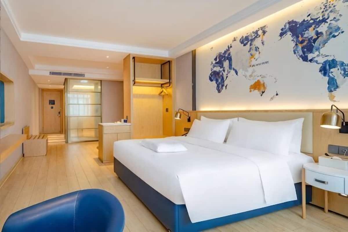 Camera d'albergo con un letto grande, una scrivania, una sedia, una mappa del mondo appesa al muro e un bagno visibile attraverso una porta in vetro.