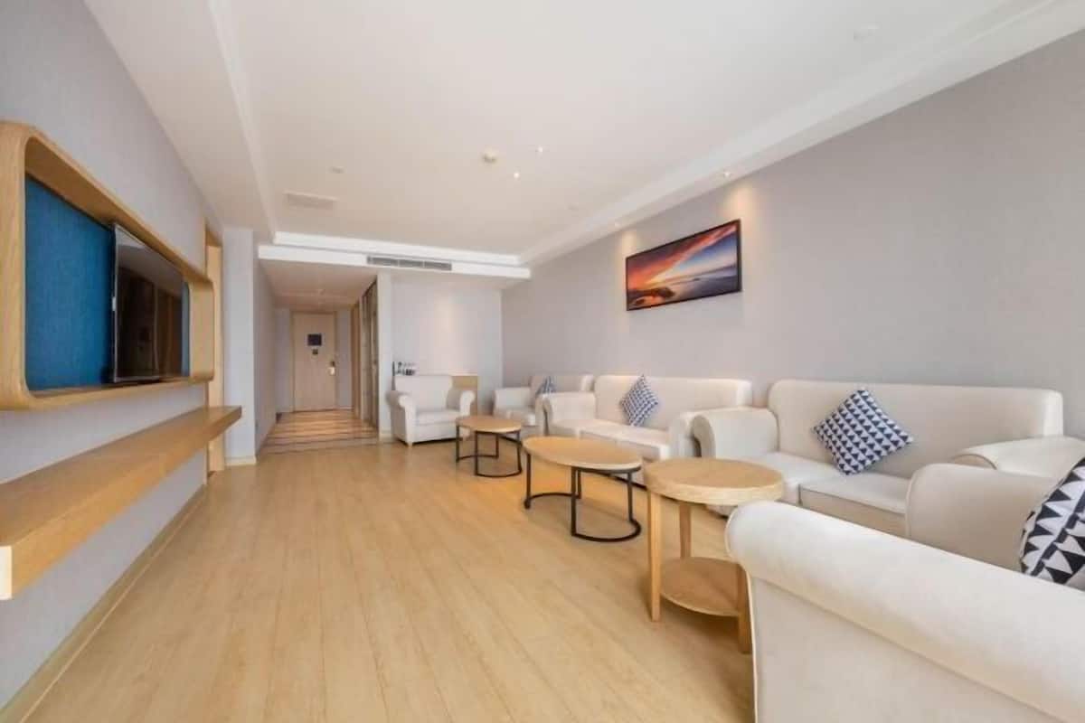 Una hall d'hotel moderna con pavimento in legno, divani bianchi e tavolini rotondi.