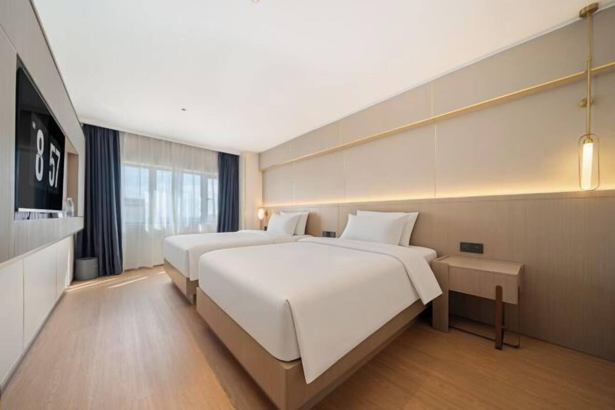 A modern hotel room with two beds, a desk, and a TV.