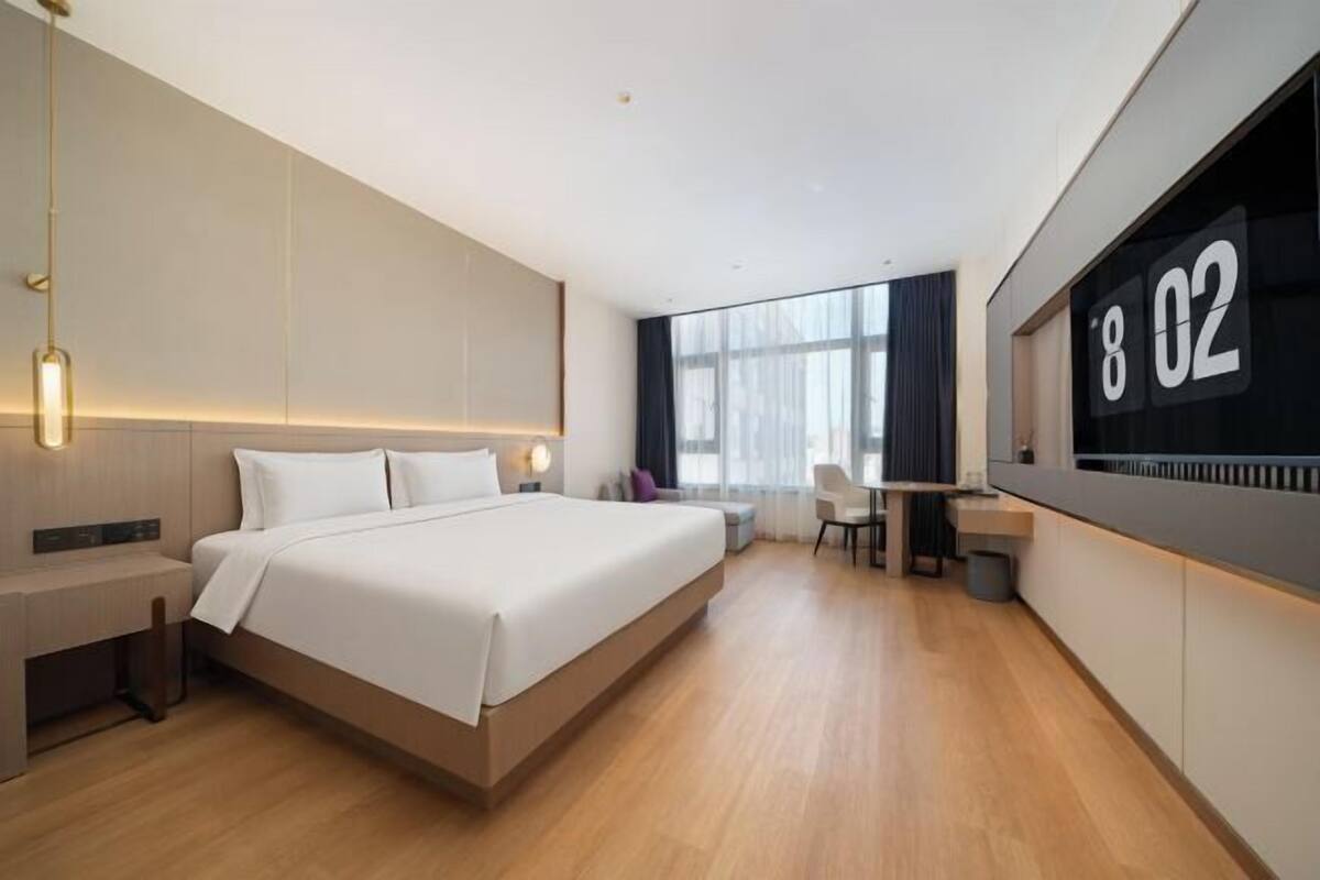A modern hotel room with a large bed, bedside tables, a desk, and a large window.