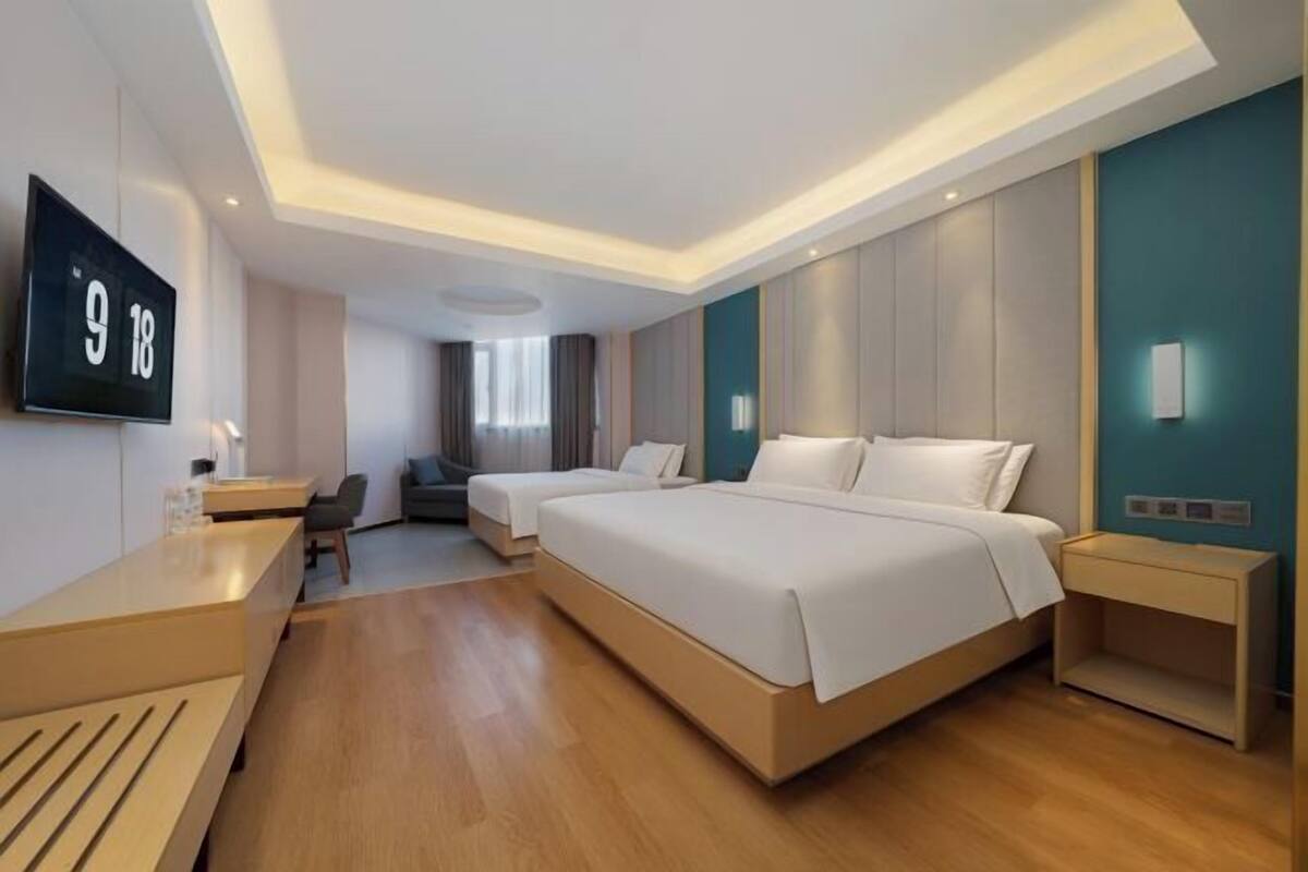 A modern hotel room with a large bed, a desk, a chair, and a TV mounted on the wall.