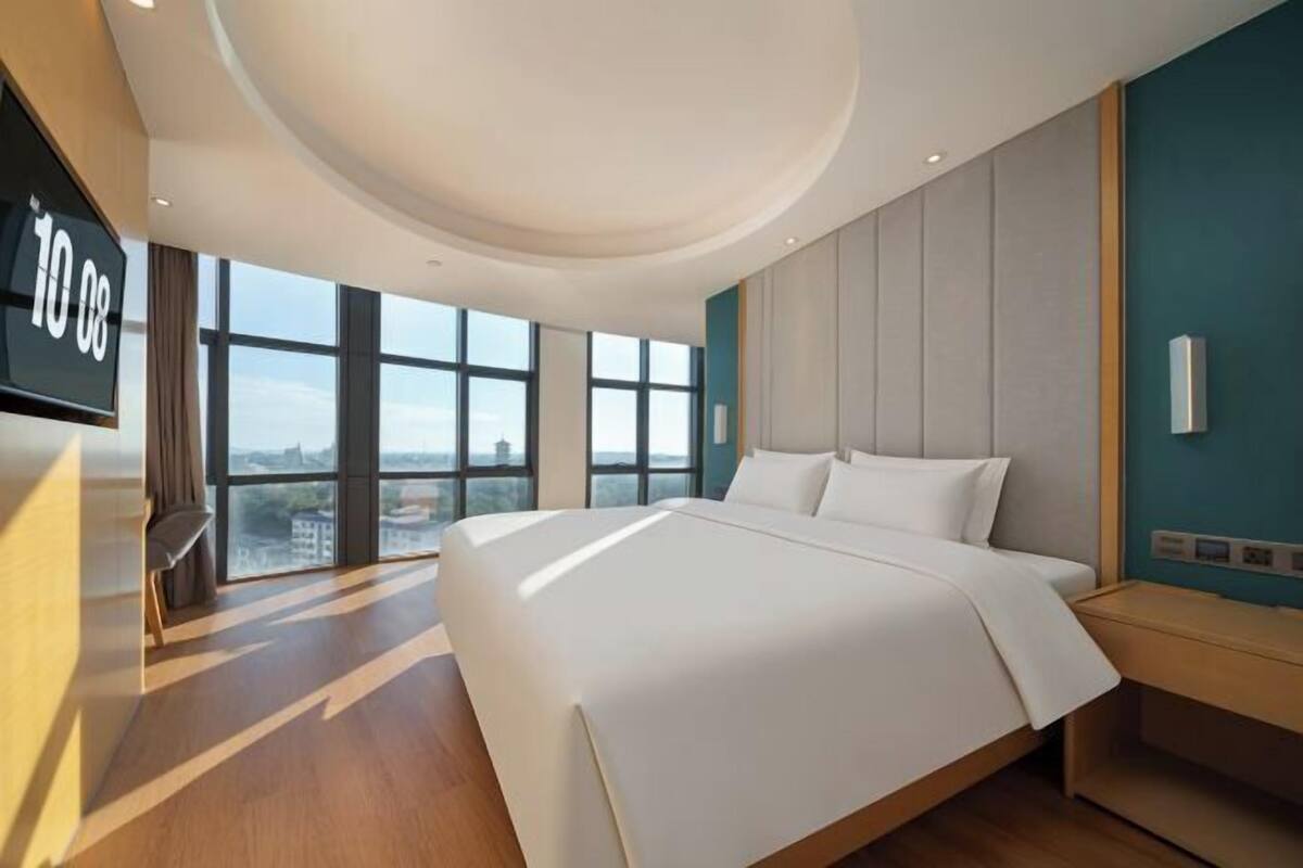 A modern hotel room with a large bed, a TV, and a city view.