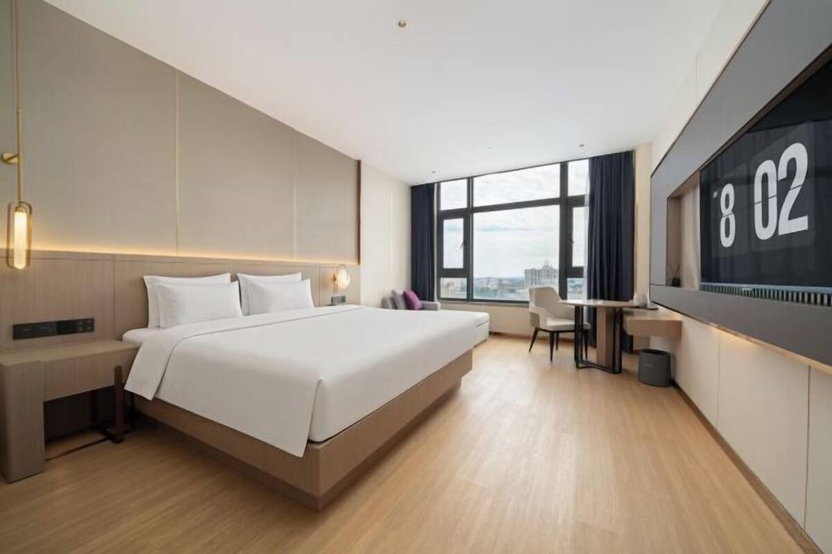 A modern hotel room with a large bed, a desk, and a city view through the window.