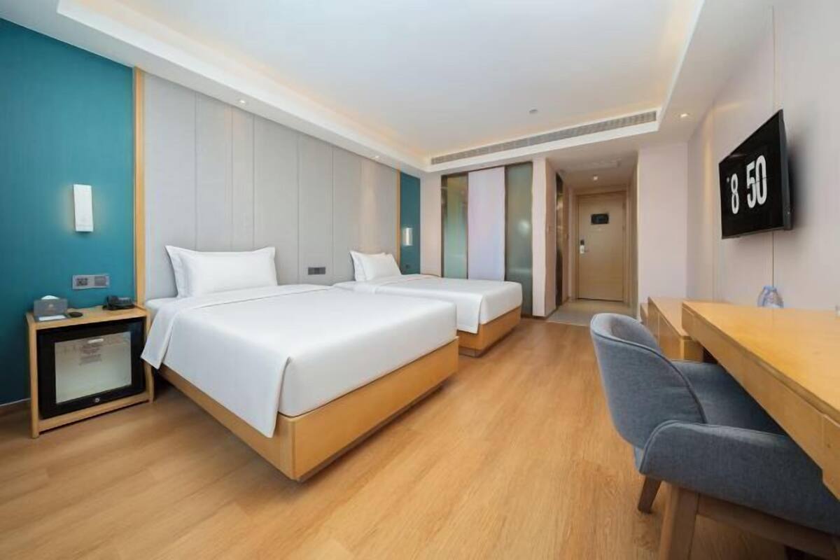 A hotel room with two beds, a desk, and a TV.