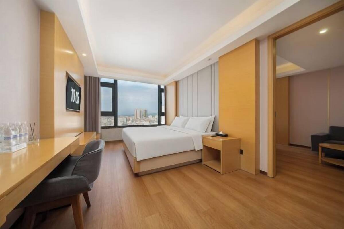 A modern hotel room with a large bed, a desk, and a view of the city.