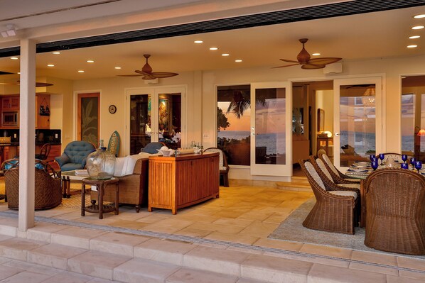 A spacious living area with a large sofa, a wooden coffee table, wicker chairs, and a dining table set with blue glassware.