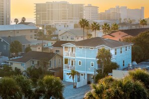 Un immeuble résidentiel à plusieurs étages doté d’un balcon, entouré de palmiers et d’autres maisons.