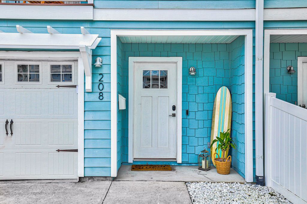 A house with a turquoise exterior, a white garage door, and a surfboard leaning against the wall.