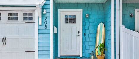 A house with a turquoise exterior, a white garage door, and a surfboard leaning against the wall.