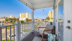 A balcony with a chair and a patterned rug, overlooking a street with cars and buildings.