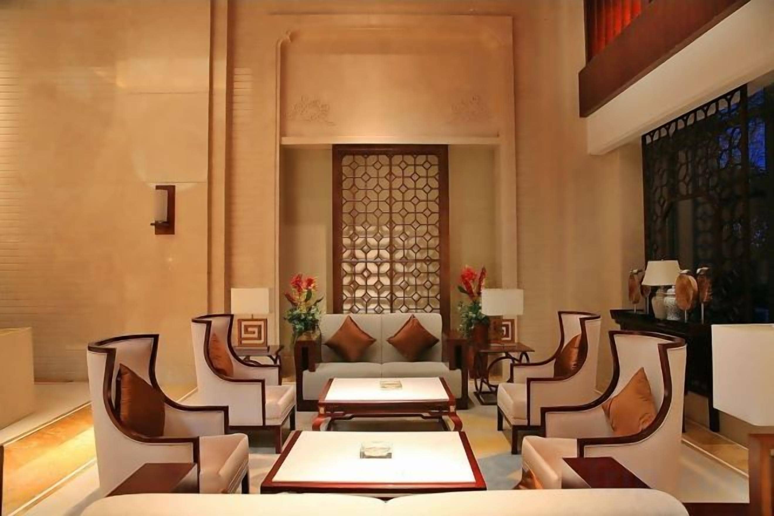 A hotel lobby with a central seating area, a decorative wall, and a view of the outside.