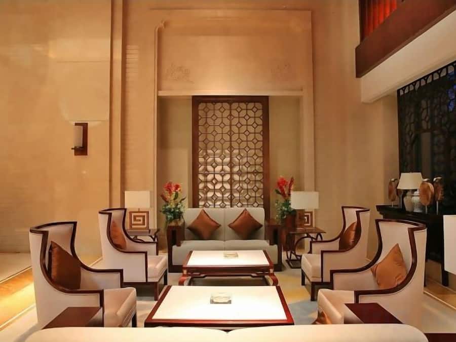 A hotel lobby with a central seating area, a decorative wall, and a view of the outside.