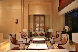 A hotel lobby with a central seating area, a decorative wall, and a view of the outside.