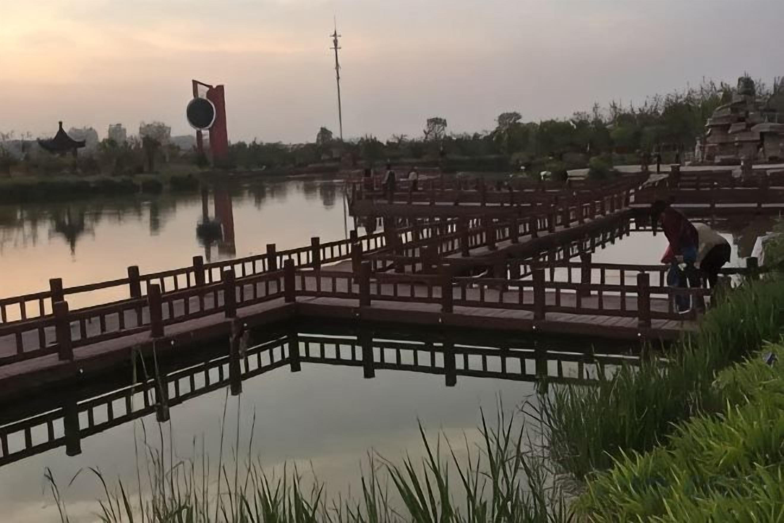 Ruhige Wasserfläche mit einer Holzbrücke und einer pagodähnlichen Struktur im Hintergrund.