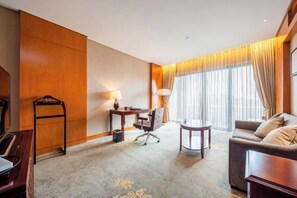Una habitación de hotel con un panel de madera en la pared, un escritorio con lámpara, un sofá y una mesa redonda.
