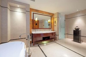 Un baño moderno con una bañera independiente, un tocador doble con un espejo grande y un florero sobre un pedestal.