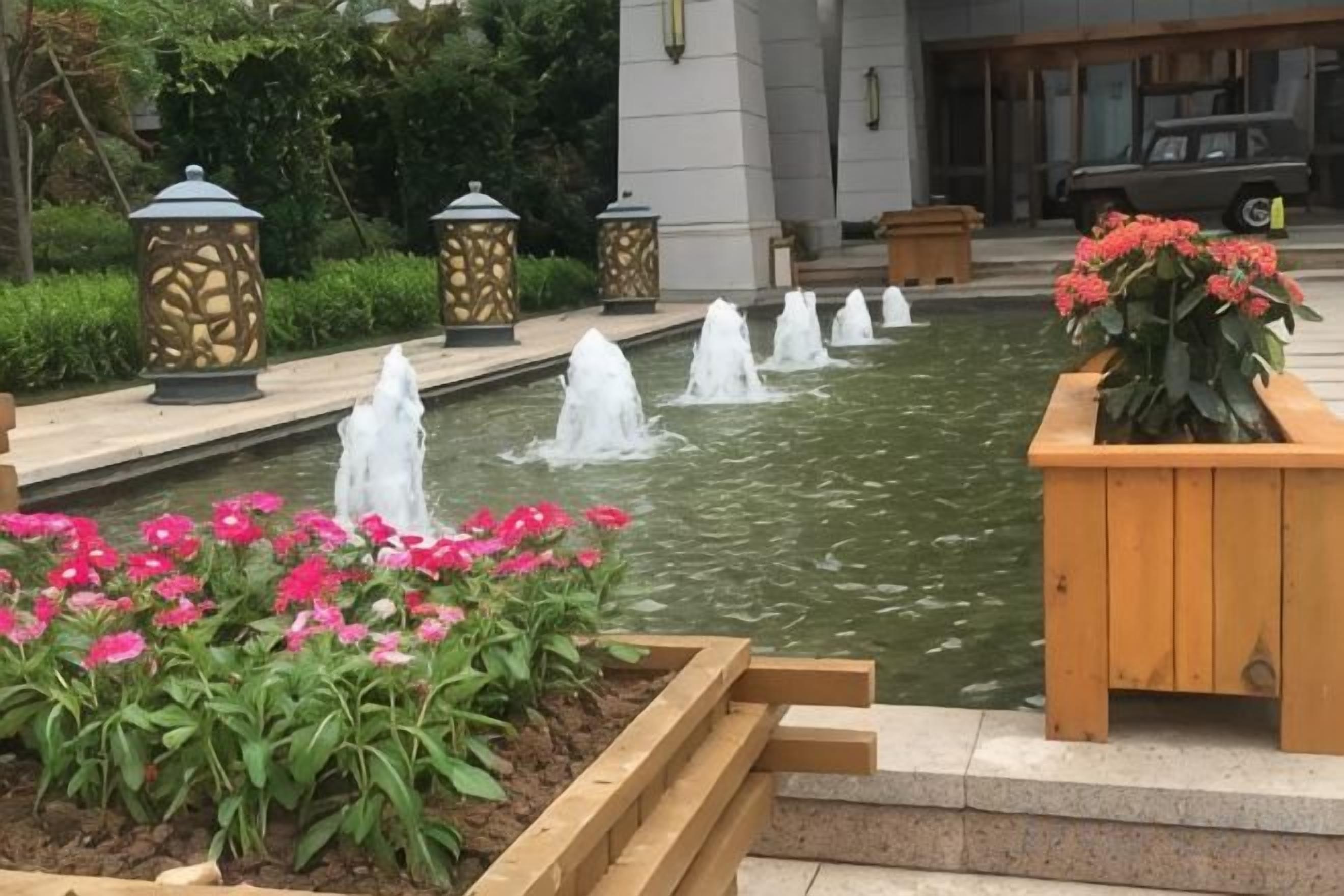 Uma fonte com várias cascatas, cercada por canteiros de flores e jardineiras de madeira.