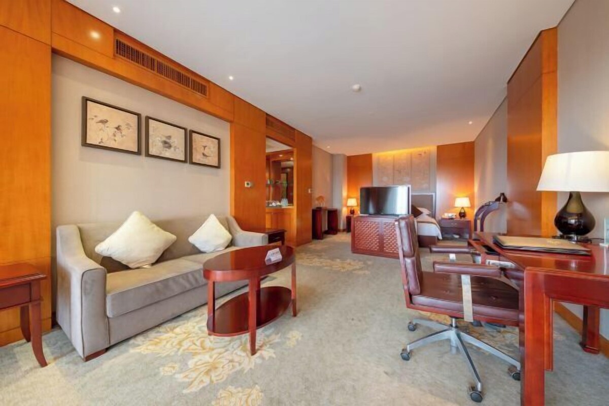 Habitación de hotel con sofá, escritorio con silla, televisor y cuadros en la pared.
