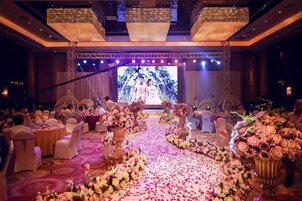 A wedding reception with a stage, floral arrangements, and round tables.