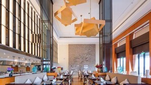 Un restaurante moderno con techos altos, lámparas geométricas en el techo y una pared central con una escultura metálica.