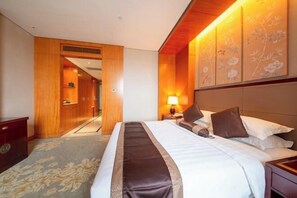 Habitación de hotel con una cama grande, cabecera de madera, una mesita de noche, una lámpara y vistas a un pasillo.