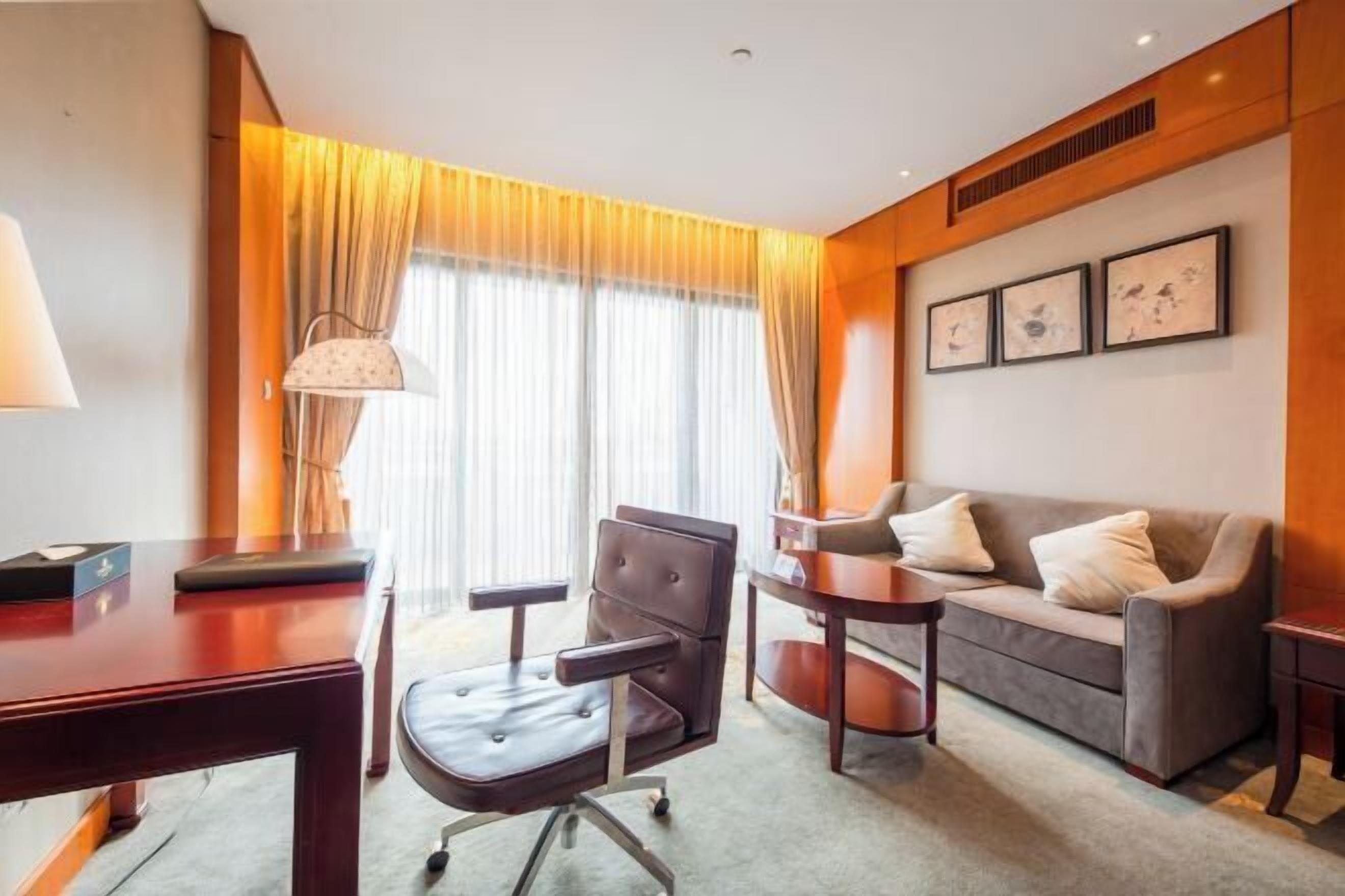 A hotel room with a desk, office chair, sofa, and a large window with curtains.