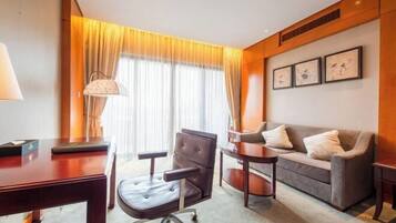 A hotel room with a desk, office chair, sofa, and a large window with curtains.