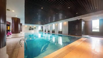 An indoor swimming pool with a tiled floor, a metal ladder, and a ceiling with a linear pattern.