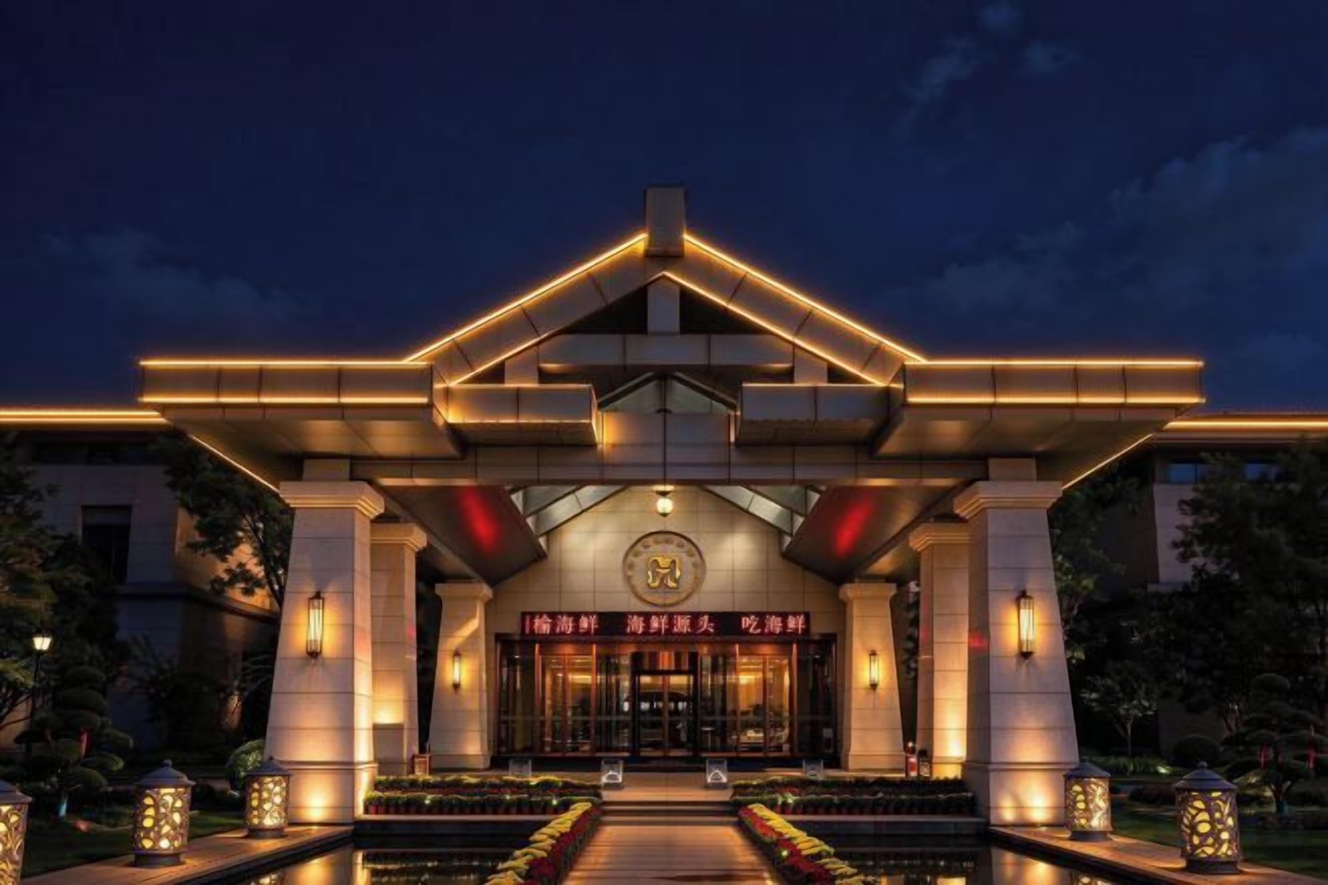 Entrada de un hotel con un dosel llamativo, fachada bien iluminada y una puerta de acceso formal.