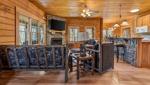 L’intérieur d’une cabane en rondins, avec une cheminée en pierre, des meubles en bois et un coin cuisine.