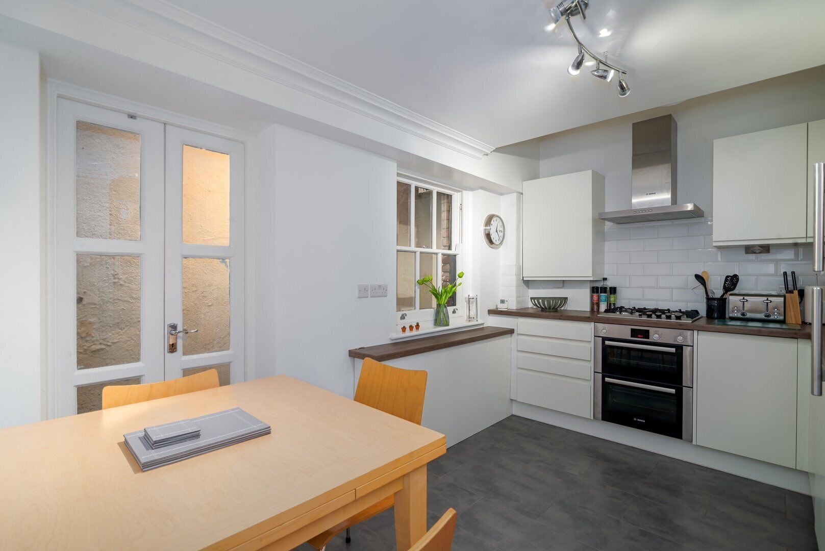 A modern kitchen with white cabinets, a wooden dining table, and a built-in oven.