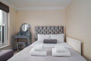 Ein Hotelzimmer mit einem großen Bett, einem Nachttisch mit Lampe, einem Spiegel und einem Fenster.