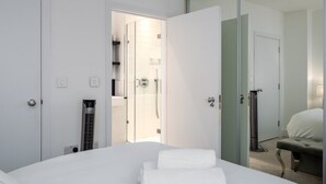 Et moderne hotelværelse med en stor seng, brusekabine i glas og et walk-in closet.