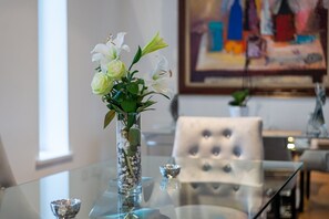 Une table en verre sur laquelle est posé un vase rempli de fleurs blanches et de feuilles vertes.