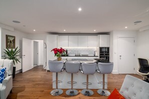 Une cuisine moderne avec des meubles blancs, un îlot central doté de tabourets et une plante en pot aux fleurs rouges.
