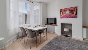 A modern living room with a dining table, chairs, a TV, and a fireplace. - GuestReady - Beautiful Apt in Clapham (London)