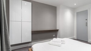 A modern hotel room with a large bed, a wardrobe, and a small seating area. - GuestReady - Beautiful Apt in Clapham (London)