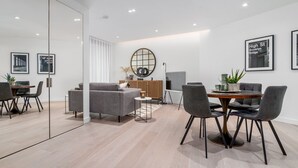 A modern interior with a dining area, sofa, and a round mirror. - GuestReady - 2BR Luxury Flat in Central London (London)