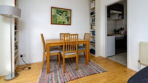 A dining area with a wooden table and chairs, a colorful rug, a bookshelf, and a kitchen visible through an open door. - GuestReady Essential - Penthouse Vibes in Peckham (London)