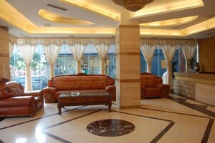 Un hall de hotel con mostrador de recepción, sofás de cuero, una mesa de centro y ventanas amplias con cortinas.