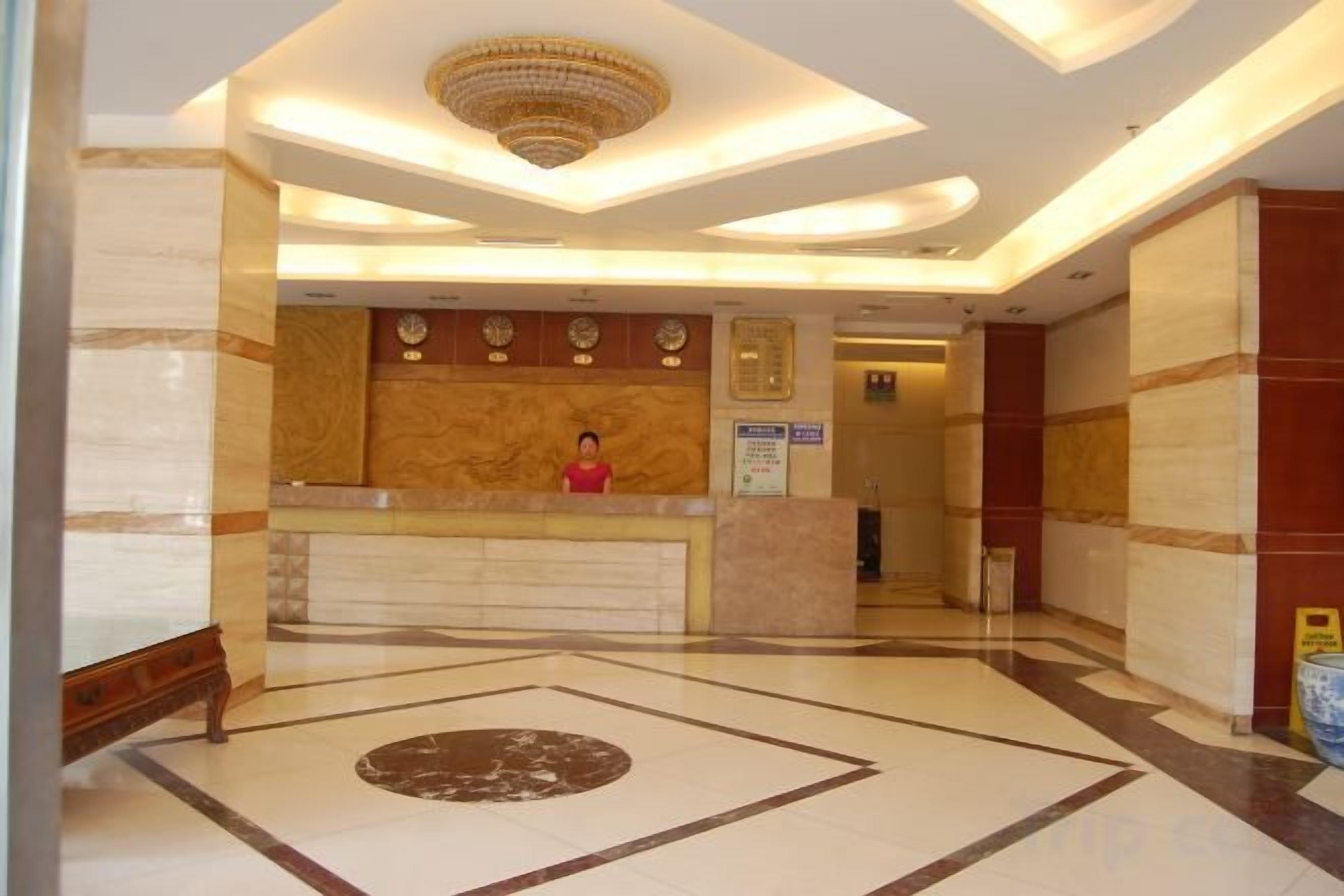 A hotel reception area with a marble floor, a reception desk, and a chandelier.