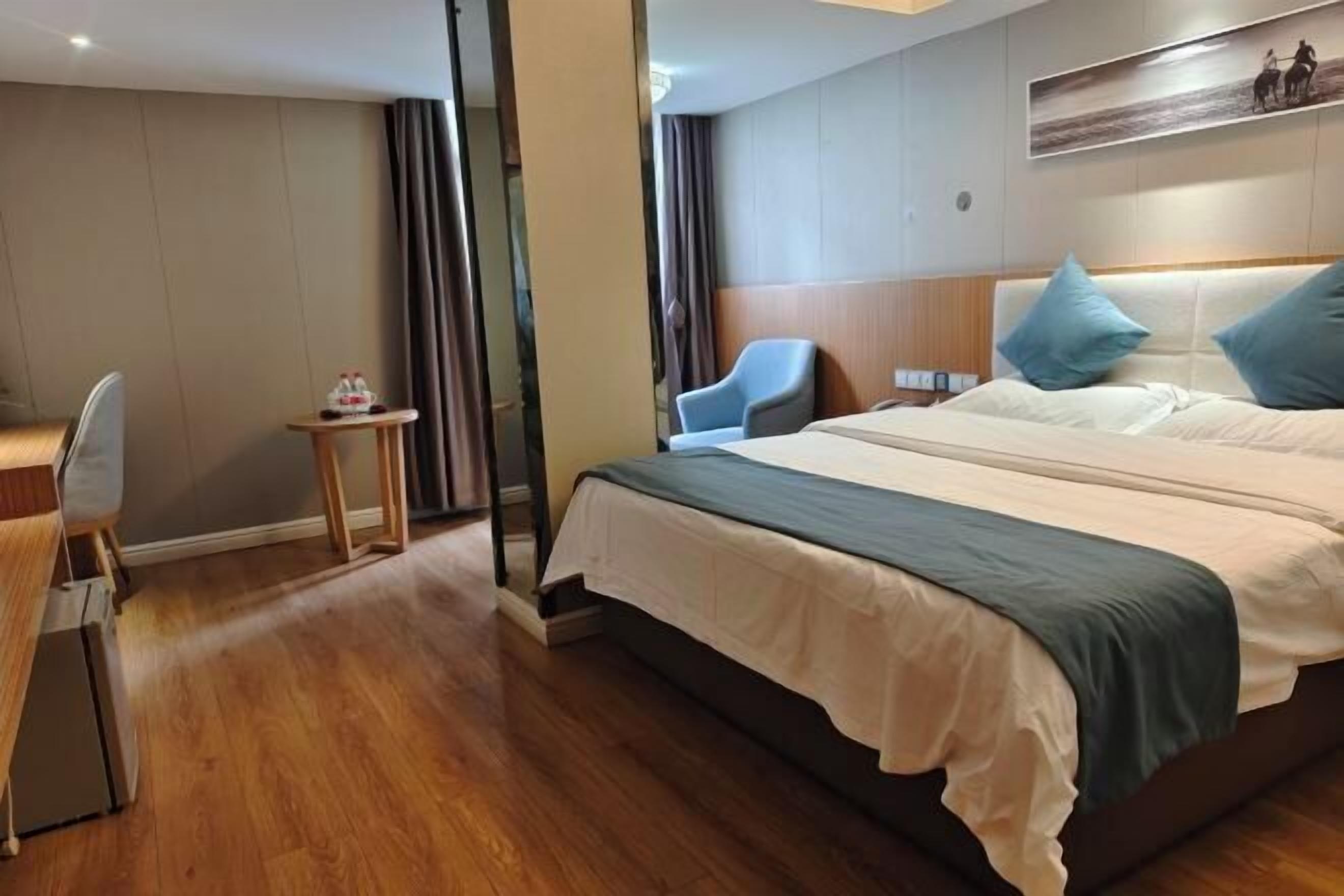 Una habitación de hotel con cama, escritorio, silla y una mesita con una botella.