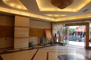 Un hall de hotel con mostrador de recepción, un gran candelabro y vistas a la calle.