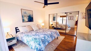 Ein Schlafzimmer mit einem Bett, Nachttischen, einem Deckenventilator, einem großen Spiegel und einem Gemälde an der Wand.
