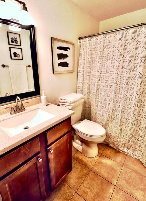 A bathroom with a sink, mirror, toilet, and shower curtain.