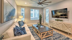 A living room with a sofa, coffee table, TV, and ceiling fan. - Modern Irvine Condo w/ Pool - 7 Mi to Beach! (Irvine)
