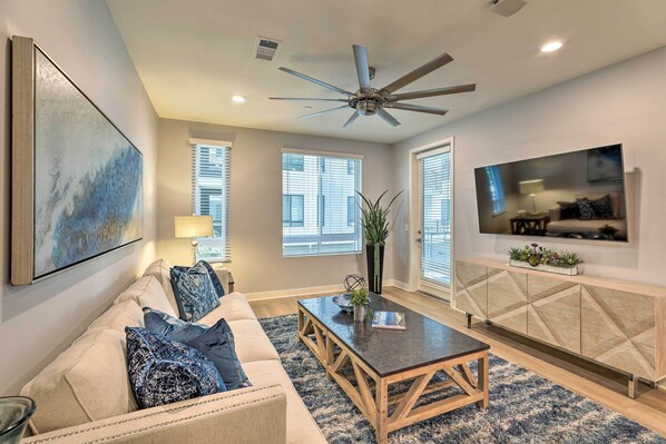 A living room with a sofa, coffee table, TV, and ceiling fan. - Modern Irvine Condo w/ Pool - 7 Mi to Beach! (Irvine)