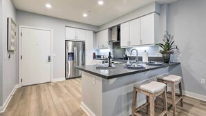 A modern kitchen with a central island, stainless steel appliances, and wooden bar stools. - Modern Irvine Condo w/ Pool - 7 Mi to Beach! (Irvine)